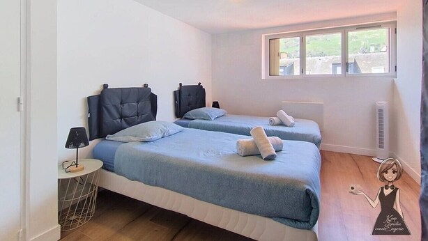 Et værelse med to senge, et lille bord med en lampe, et vindue med udsigt og en loftlampe.