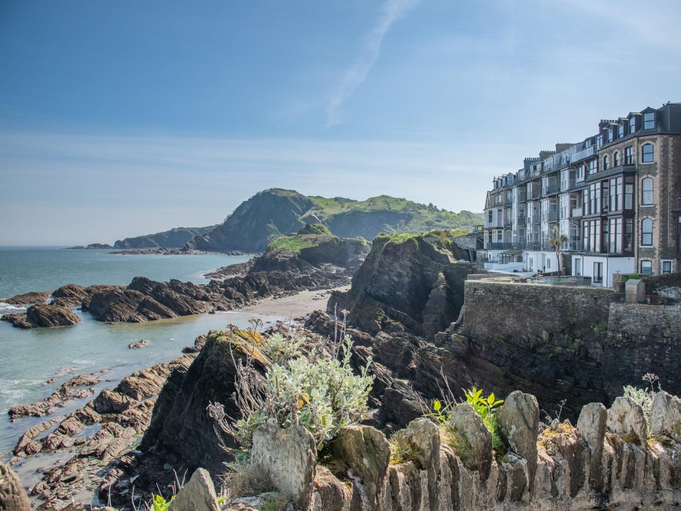 A coastal scene with rocky terrain, a beach, and a building with multiple windows and balconies.
