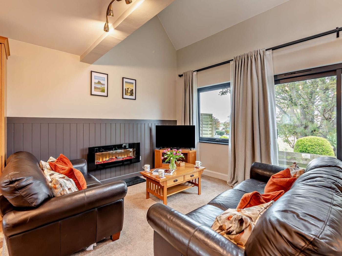 A modern living room with leather sofas, a flat-screen TV, a fireplace, and a large window with curtains.