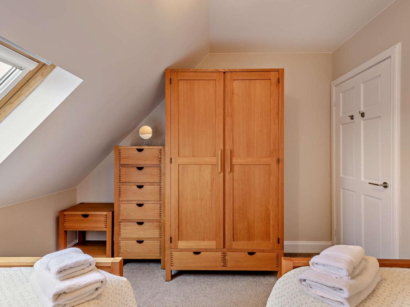 Una camera da letto con un'armadio in legno, un comodino, uno specchio e una finestra.