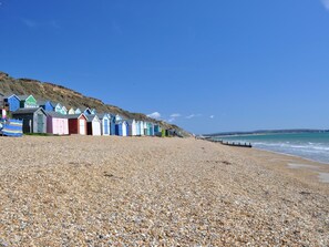 Une plage de galets, avec des cabanes de plage aux couleurs vives et un ciel dégagé.