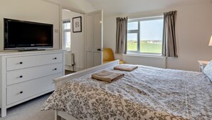 Une chambre à coucher avec un lit, un téléviseur posé sur une commode, une fenêtre avec des rideaux et une vue sur l’extérieur.