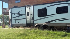 A white RV with 'Velite' branding parked in front of a wooden building. - Quaint 1 bed RV, on the lake. Sleeps 6-7 (McLoud)