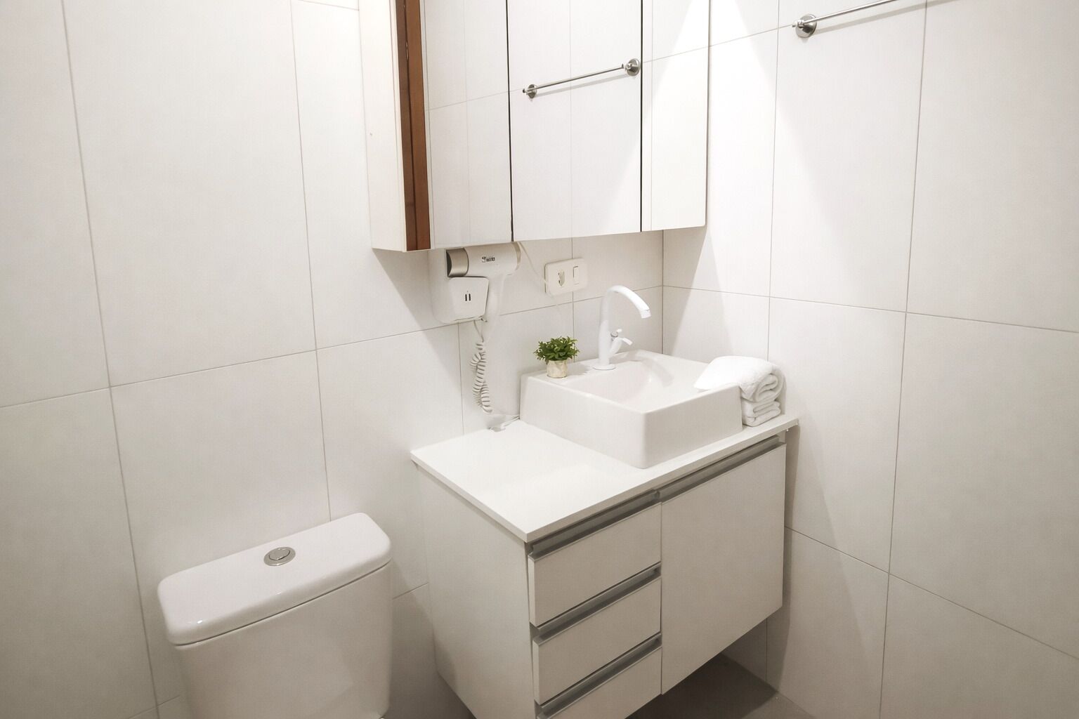 Ein kleines, weißes Badezimmer mit Toilette, Waschbecken, Spiegel und Schrank.