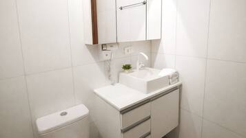Ein kleines, weißes Badezimmer mit Toilette, Waschbecken, Spiegel und Schrank.