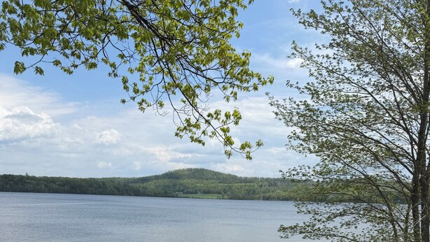 Ein Balkon mit zwei Adirondack-Stühlen, Blick auf einen See, einer Geländer und eine ferne Hügelkulisse.