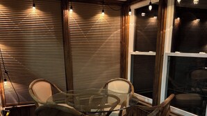 Ein Zimmer mit einem Glastisch, umringt von Korbstühlen, einem gemusterten Teppich und Holzjalousien.