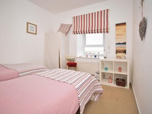 A bedroom with two beds, a radiator, a window with a view, and a shelf with decorative items. - 3 Bed in Seahouses (oc-cn097) (Seahouses)