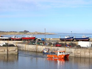 A harbor with several boats docked, a concrete breakwater, and a distant castle on the horizon. - 3 Bed in Seahouses (oc-cn097) (Seahouses)
