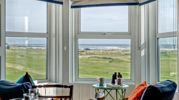 Ein Zimmer mit Blick auf den Strand, ein Tisch mit Stühlen und ein kleiner runder Tisch mit einem Buch und zwei Tassen.