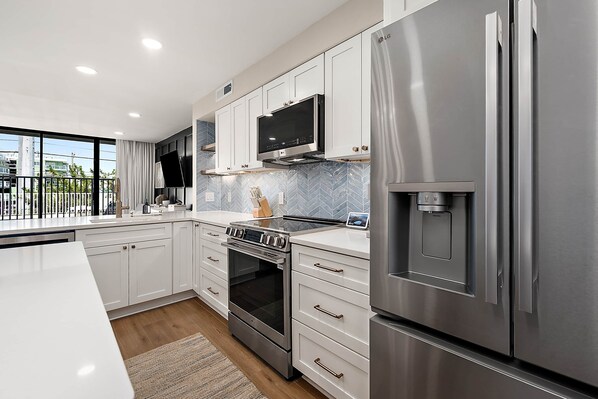 A modern kitchen with stainless steel appliances, white cabinetry, and a large window. - Ocean Side Condo | Steps to the Beach (Ocean City)
