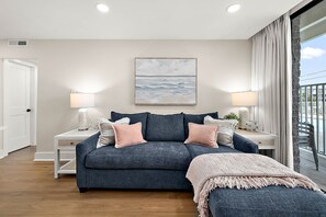 A modern bedroom with a large bed, bedside lamps, a painting, and a view of the outdoors. - Ocean Side Condo | Steps to the Beach (Ocean City)