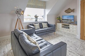 Ein modernes Wohnzimmer mit einem Ecksofa, einem Fernseher und einem dekorativen Wandbild mit Fischen.