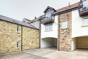 A stone building with a balcony, a garage, and a clear sky. - 2 Bed in Seahouses (oc-cn166) (Seahouses)