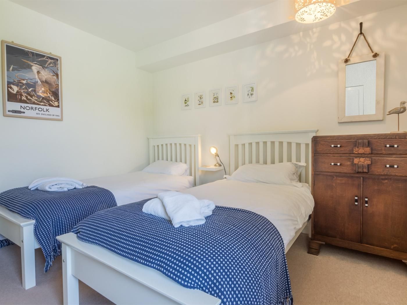 A bedroom with two beds, a wooden dresser, a wall-mounted mirror, and a poster.