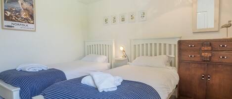 A bedroom with two beds, a wooden dresser, a wall-mounted mirror, and a poster.