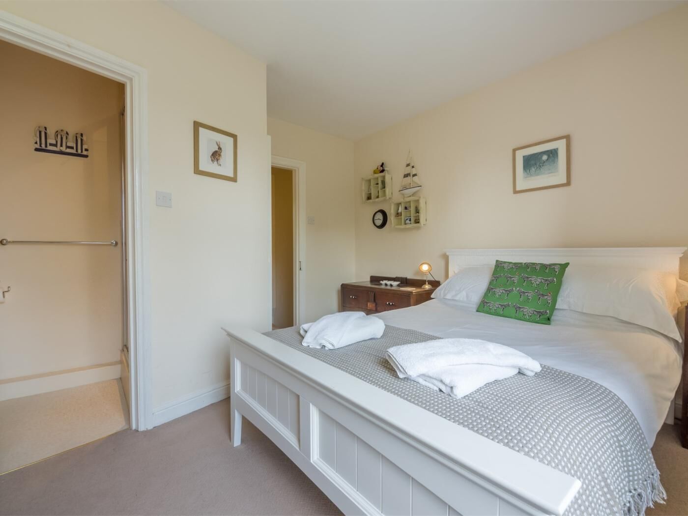 Une chambre à coucher comprenant un lit, une table de chevet, une commode, une porte et un mur orné d’une horloge et de tableaux encadrés.