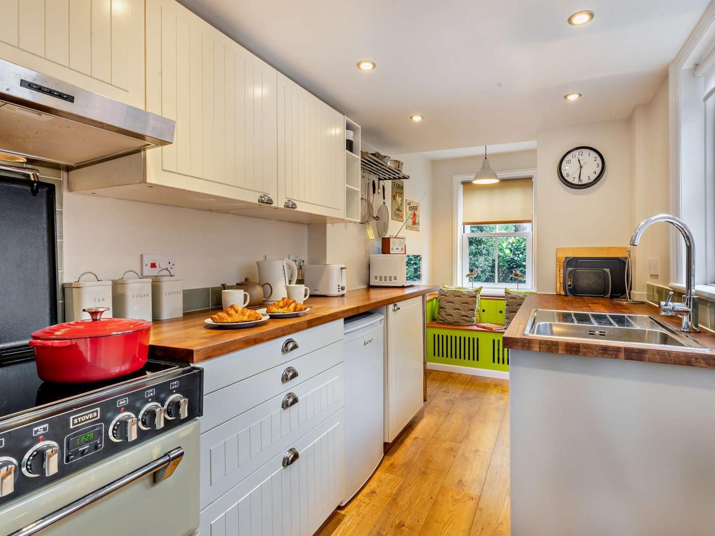 Una cocina moderna con armarios blancos, una estufa roja y un ventanal con vistas a zonas verdes.