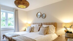 Una camera da letto con un letto grande, lampade da comodino, un comodino in legno, uno specchio e una finestra con tende.