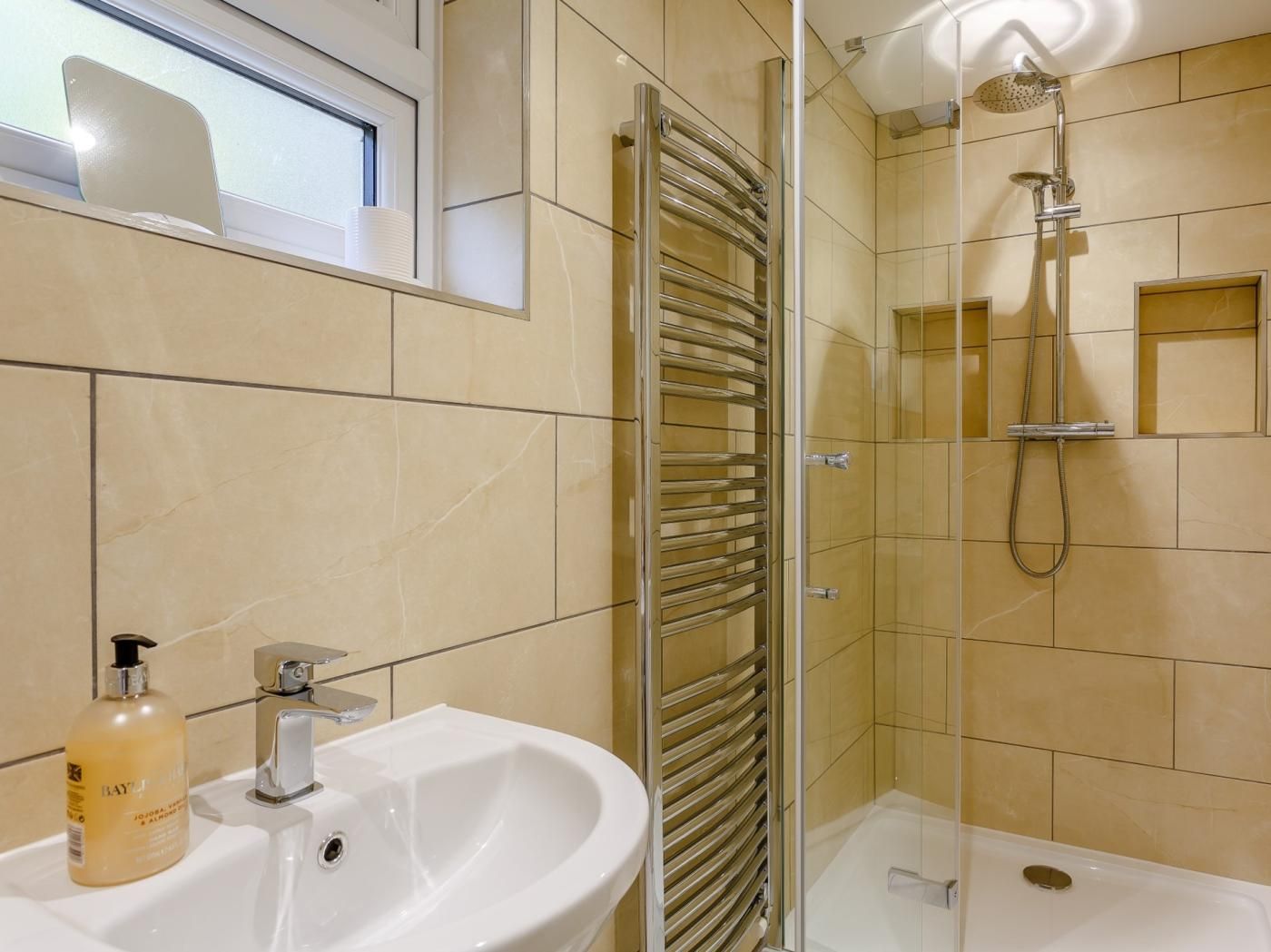 A bathroom with a glass-enclosed shower, a white sink, and a bottle of lotion.