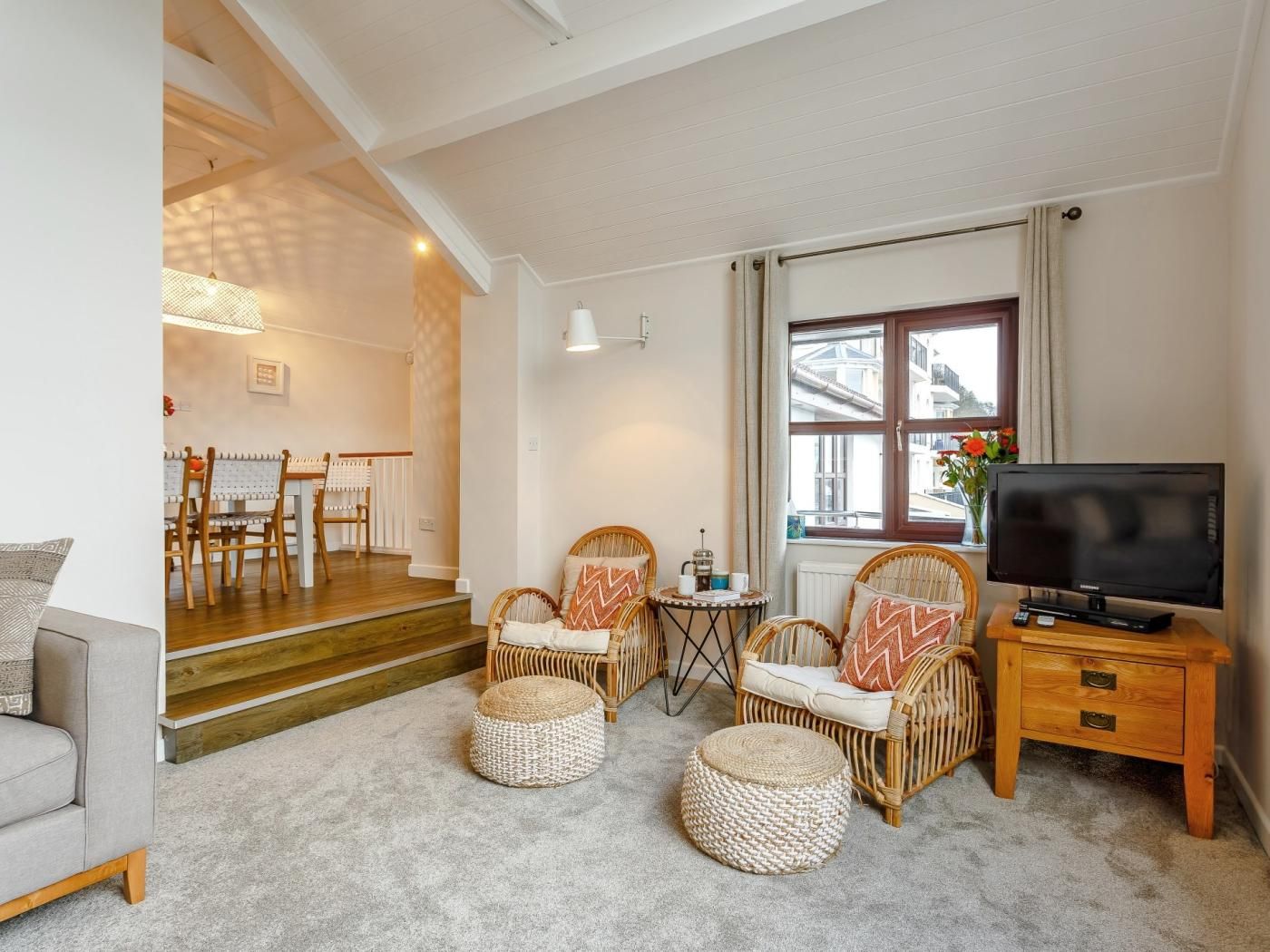 Un salon moderne doté d’un téléviseur à écran plat, de meubles en osier, d’un coin repas avec des chaises en bois et d’un escalier menant à un autre niveau.