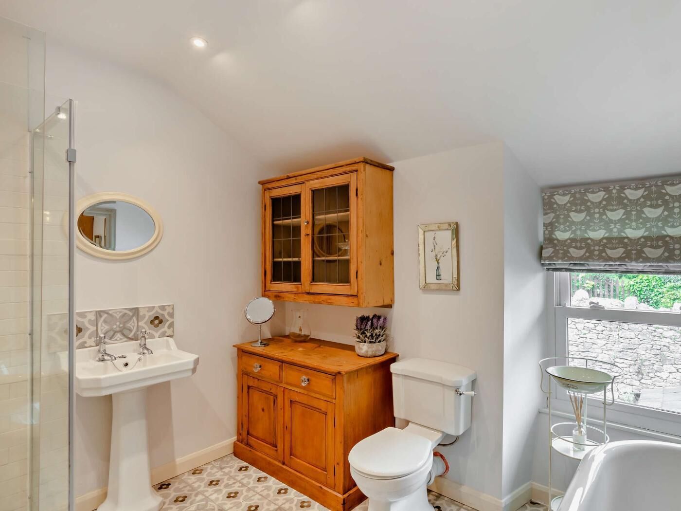Un baño con un mueble de madera, un lavabo pedestal, un inodoro y una ventana con vistas.