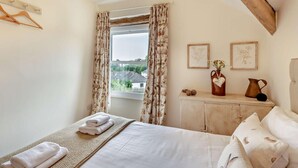 Een slaapkamer met een bed, een raam met gordijnen, een nachtkastje met een vaas, en een muur met ingelijste foto's.