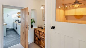 Een gang die uitkomt in een keuken, met een houten kast en een hangende lamp.