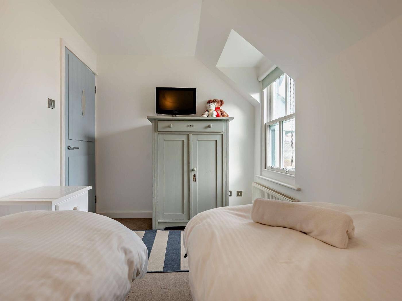 Une chambre avec deux lits, un téléviseur posé sur un meuble, une fenêtre et une porte.