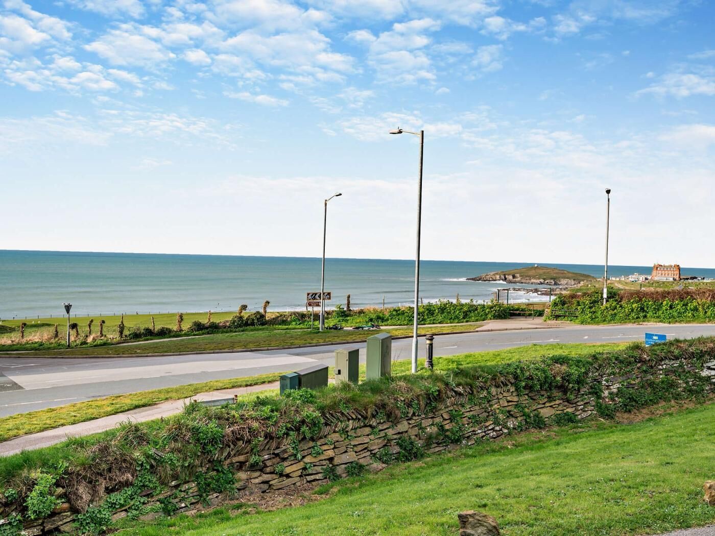 Une route côtière bordée de lampadaires, un mur de pierre et une vue sur la mer.