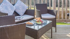 Une terrasse dotée de meubles en osier, d’une table en verre et d’une assiette de fruits et de pâtisseries.
