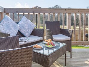Eine Terrasse mit Korbmöbeln, einem Glastisch und einer Platte mit Obst und Gebäck.
