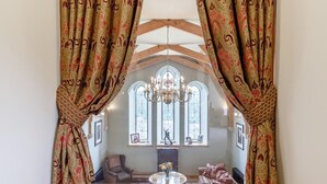 A room with a large window, a chandelier, and a fireplace. - 4 Bed in Gunnislake (oc-77480) (Latchley)