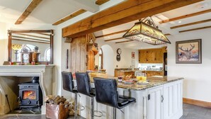 A kitchen with a central island, bar stools, a wood-burning stove, and a large mirror. - 4 Bed in Gunnislake (oc-77480) (Latchley)