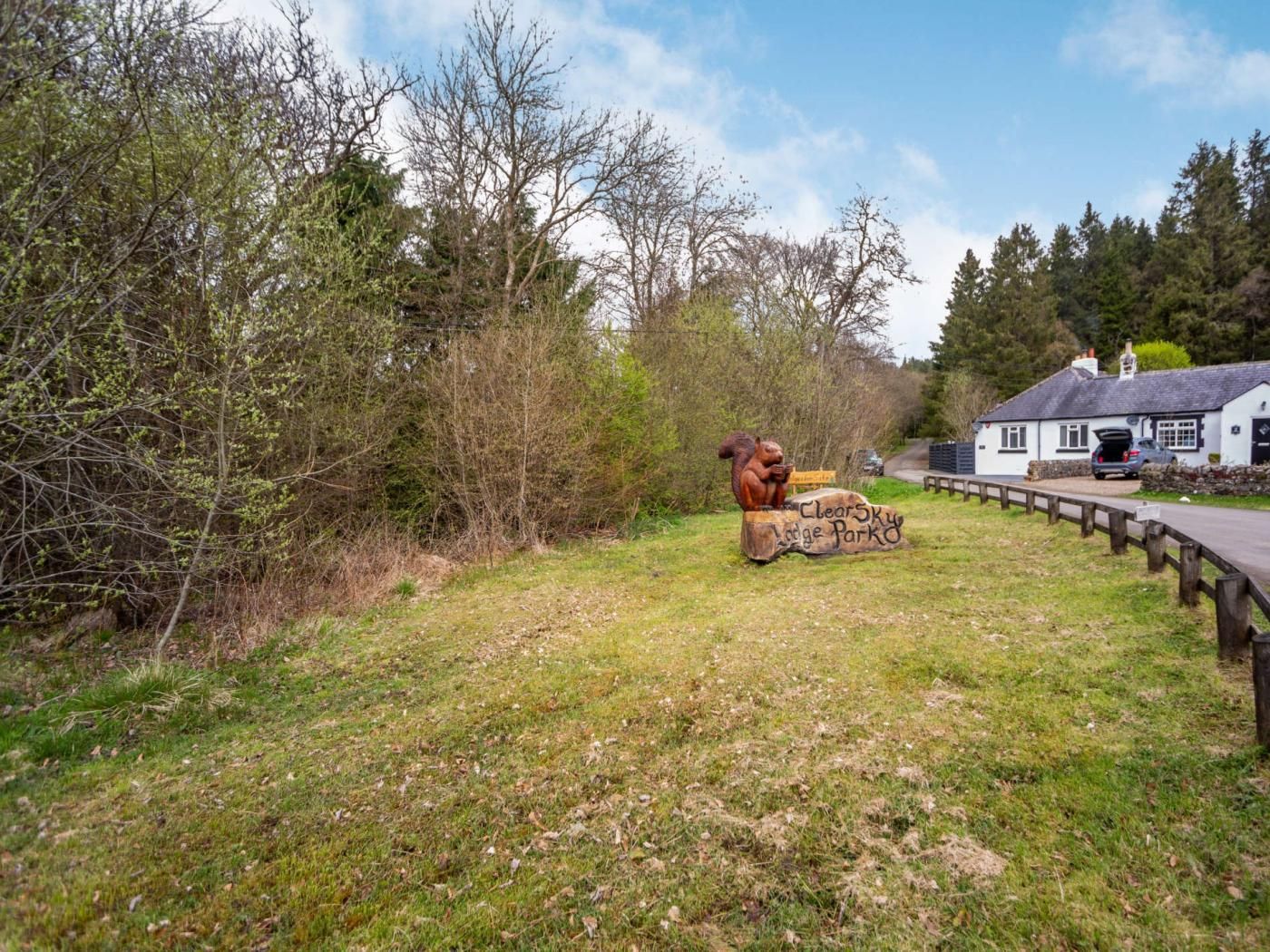 Een rustieke buitenruimte met een houten bord waarop 'Clear Sky Lodge Park' staat en een beeldhouwwerk van een eekhoorn.