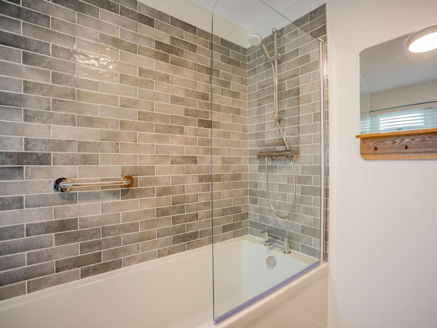 A bathroom with a glass-enclosed shower, a bathtub, and a tiled wall.