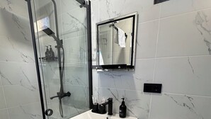 Un bany amb dutxa de vidre, un lavabo blanc amb calaixeria de fusta i un vàter blanc.