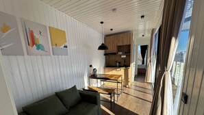 Zona d'estar moderna amb sofà, taula de menjador i cuina al fons.