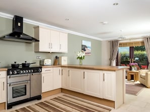A modern kitchen with a built-in oven, a stove, and a range hood. There is a dining area with a table and chairs visible through a glass door. - 4 Bed in Ystradgynlais (oc-bn343) (Cwm-twrch Isaf)