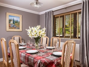Une salle à manger avec une nappe à carreaux, un vase de fleurs blanches et un tableau accroché au mur.