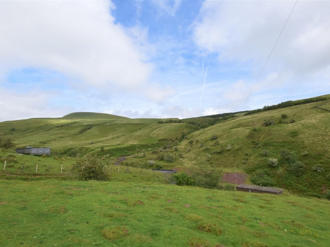 A rural landscape with rolling hills, a small building, and a fence.