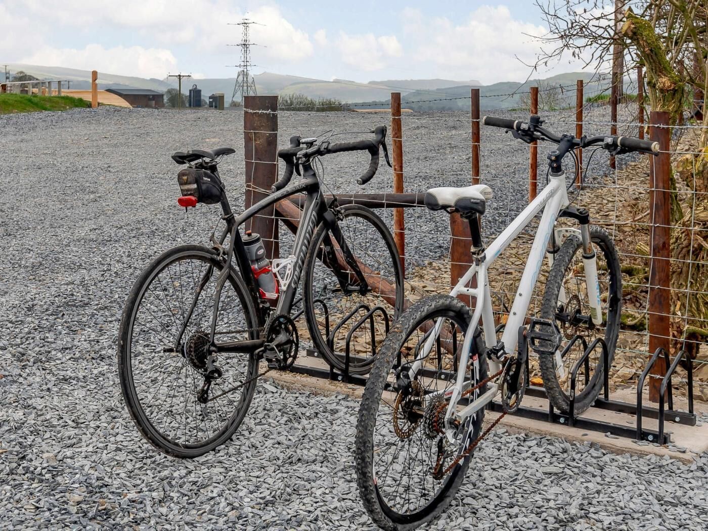 Deux vélos sont garés sur une surface de gravier, avec une clôture en arrière-plan.