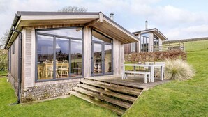 Une maison moderne dotée d’une grande porte vitrée, d’une terrasse en bois et de fondations en pierre.
