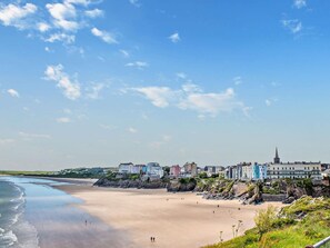 A coastal town with a sandy beach, buildings along the shore, and a clear sky. - 4 Bed in Tenby (oc-fb104) (Tenby)
