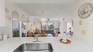 A modern kitchen with a large sink, dining area with chairs, a sofa, and a view through the window. - Ocean Village Club K35 (St. Augustine)