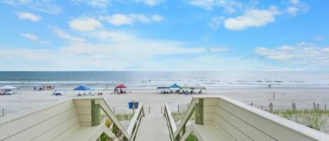 A wooden staircase leading to a beach with umbrellas and people.