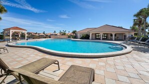 Piscina con sillas de descanso y una zona cubierta, rodeada por un patio empedrado.