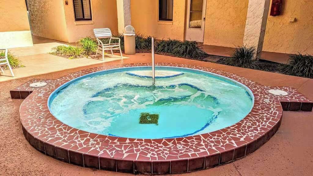 A hot tub with a mosaic tile border, surrounded by a patio area with chairs and plants.