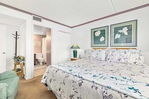 A bedroom with a large bed, a bedside table with a lamp, and a door leading to a bathroom. - New! St. Augustine Resort Condo With Free Tickets (St. Augustine)