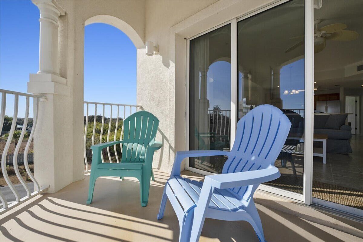 Ein Balkon mit zwei Adirondack-Stühlen, einem weißen Geländer und einer Glasgleittür, die zu einem Innenbereich führt.